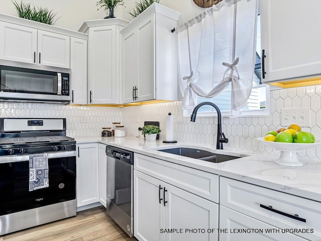 kitchen featuring stainless steel appliances, a sink, white cabinetry, tasteful backsplash, and light wood-style flooring