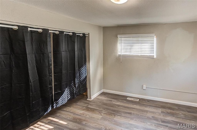 empty room with wood finished floors, a textured ceiling, and baseboards