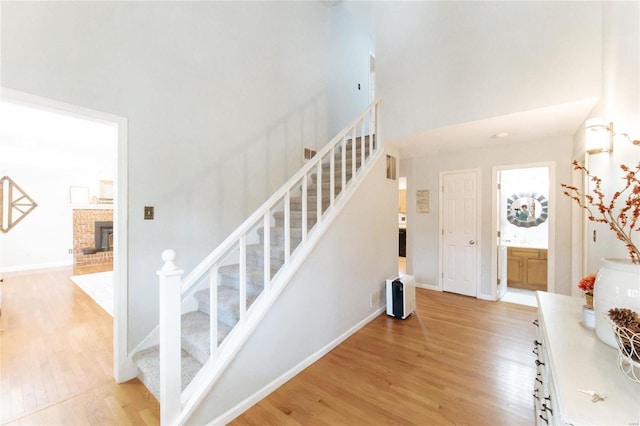 staircase with wood finished floors, a fireplace, a towering ceiling, and baseboards