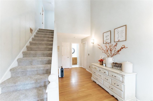 stairway featuring wood finished floors, a high ceiling, and baseboards