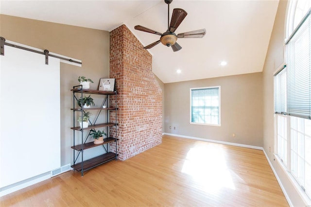 unfurnished living room featuring wood finished floors, ceiling fan, baseboards, a barn door, and high vaulted ceiling