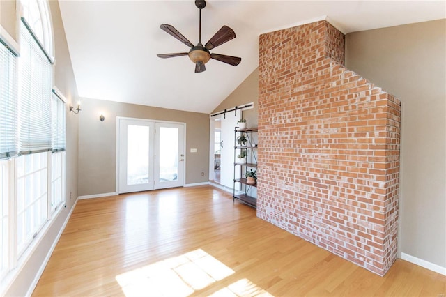 unfurnished living room with high vaulted ceiling, a barn door, light wood-style floors, baseboards, and ceiling fan