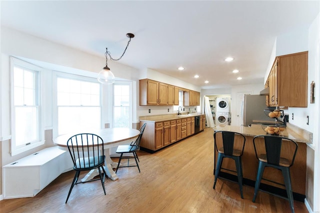 kitchen with stacked washer / dryer, a sink, brown cabinets, light wood finished floors, and recessed lighting