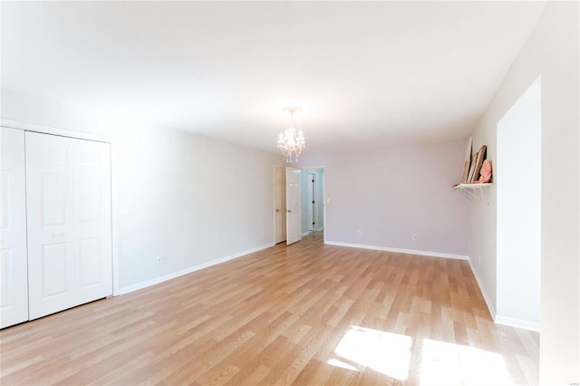 empty room featuring a chandelier, light wood-type flooring, and baseboards