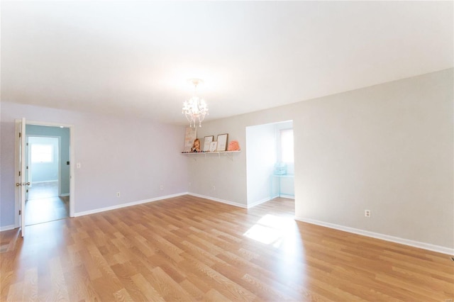 spare room with a chandelier, light wood finished floors, and baseboards