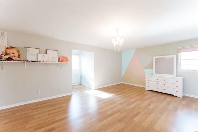 spare room with wood finished floors, a chandelier, and baseboards