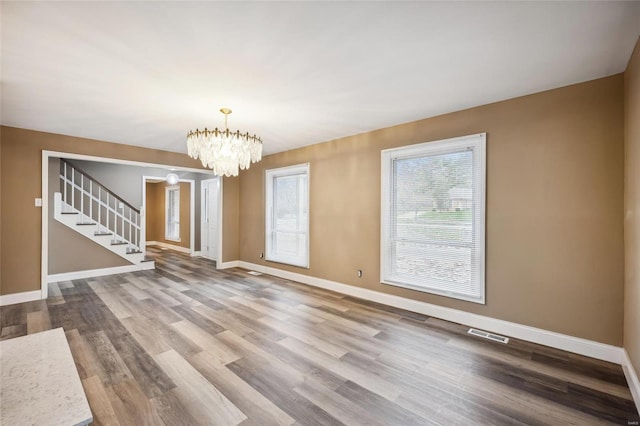 unfurnished living room with stairway, baseboards, wood finished floors, and a chandelier