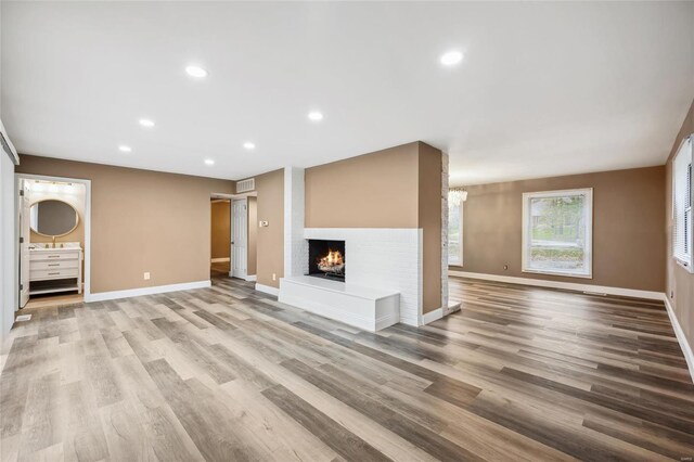 unfurnished living room with light wood-type flooring, baseboards, a multi sided fireplace, and recessed lighting