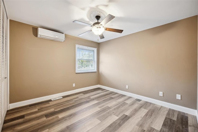 unfurnished room featuring a wall unit AC, a ceiling fan, light wood finished floors, and baseboards