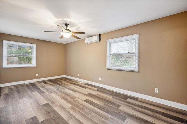 spare room featuring a wall mounted air conditioner, ceiling fan, baseboards, and wood finished floors