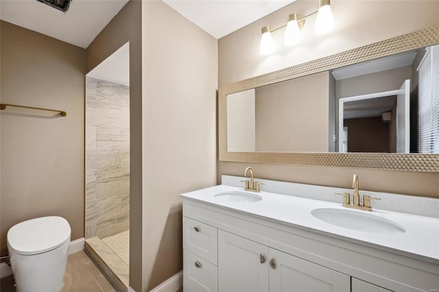 bathroom with a tile shower, toilet, double vanity, and baseboards