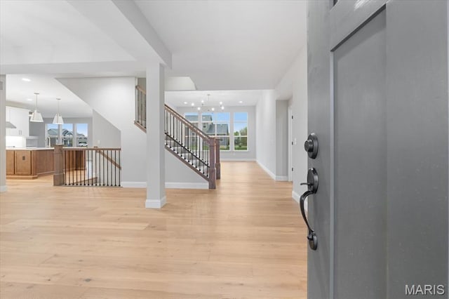 entrance foyer with baseboards, light wood-style floors, a chandelier, and stairs