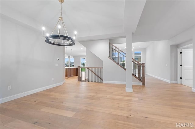 unfurnished dining area featuring a chandelier, light wood-type flooring, baseboards, and stairway
