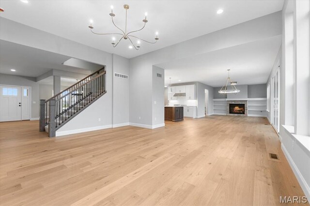 unfurnished living room with light wood-type flooring, stairs, a chandelier, a lit fireplace, and recessed lighting