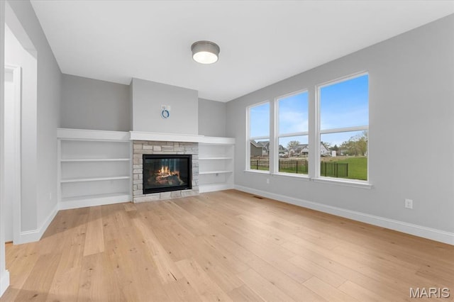 unfurnished living room featuring light wood-style floors, baseboards, a stone fireplace, and built in features