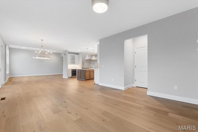 unfurnished living room featuring baseboards, light wood-style floors, recessed lighting, and beverage cooler