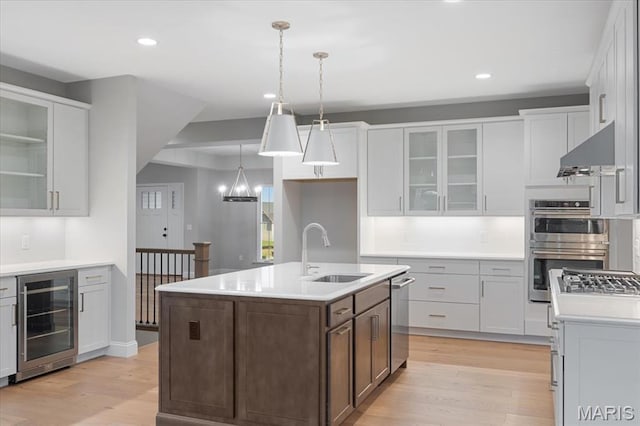 kitchen featuring wine cooler, a sink, under cabinet range hood, appliances with stainless steel finishes, and light wood-style floors