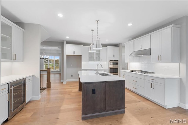 kitchen featuring wine cooler, a sink, stainless steel appliances, baseboards, and under cabinet range hood