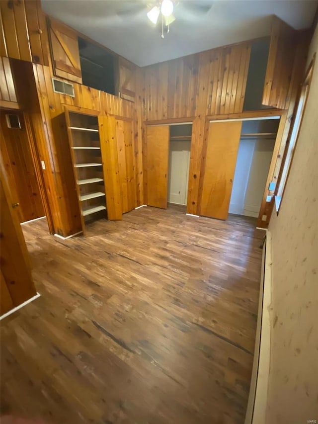 unfurnished bedroom featuring wood finished floors, wooden walls, and multiple closets
