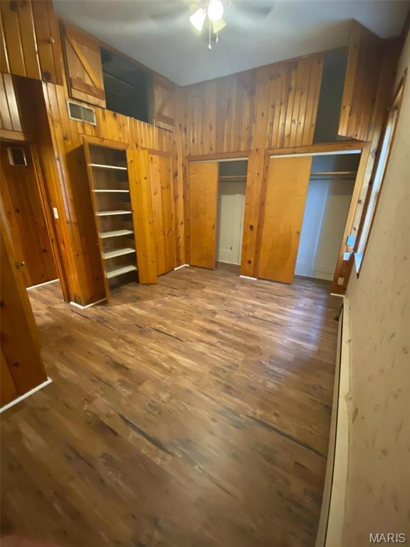 125 S 5th, Saint Charles, MO 63301 - unfurnished bedroom featuring wood finished floors, wood walls, and multiple closets