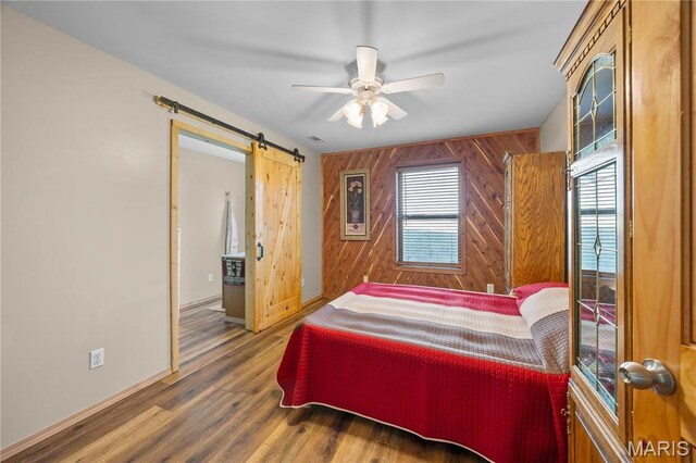 9136 Beach Dr, French Village, MO 63036 - bedroom with wood walls, a barn door, baseboards, wood finished floors, and ceiling fan