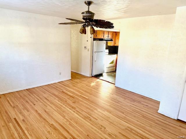 empty room with ceiling fan, light wood finished floors, and baseboards
