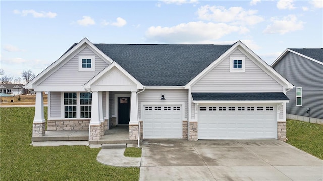 view of front facade with stone siding, driveway, a shingled roof, a porch, and a front yard