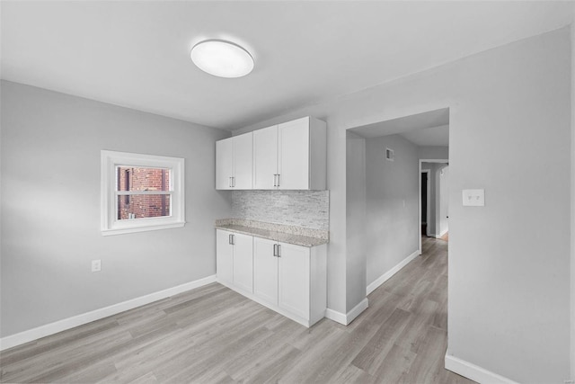 kitchen featuring light countertops, light wood-style floors, white cabinets, baseboards, and decorative backsplash