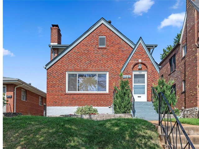 tudor-style house featuring brick siding, a chimney, and a front lawn