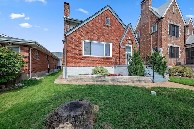 tudor house featuring a chimney, brick siding, and a front yard