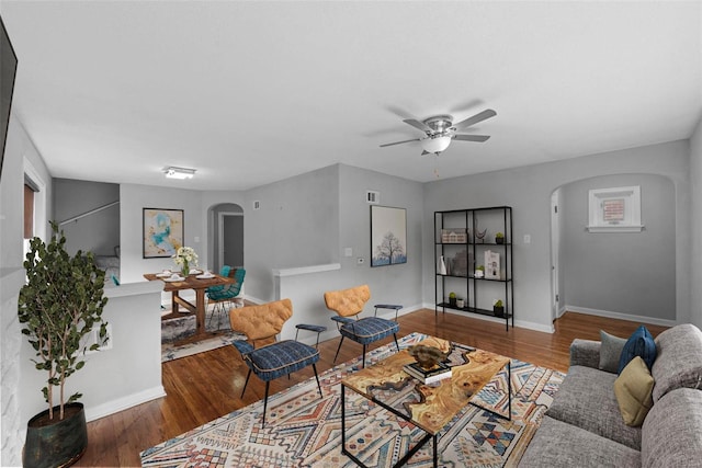 living room featuring arched walkways, a ceiling fan, wood finished floors, and baseboards