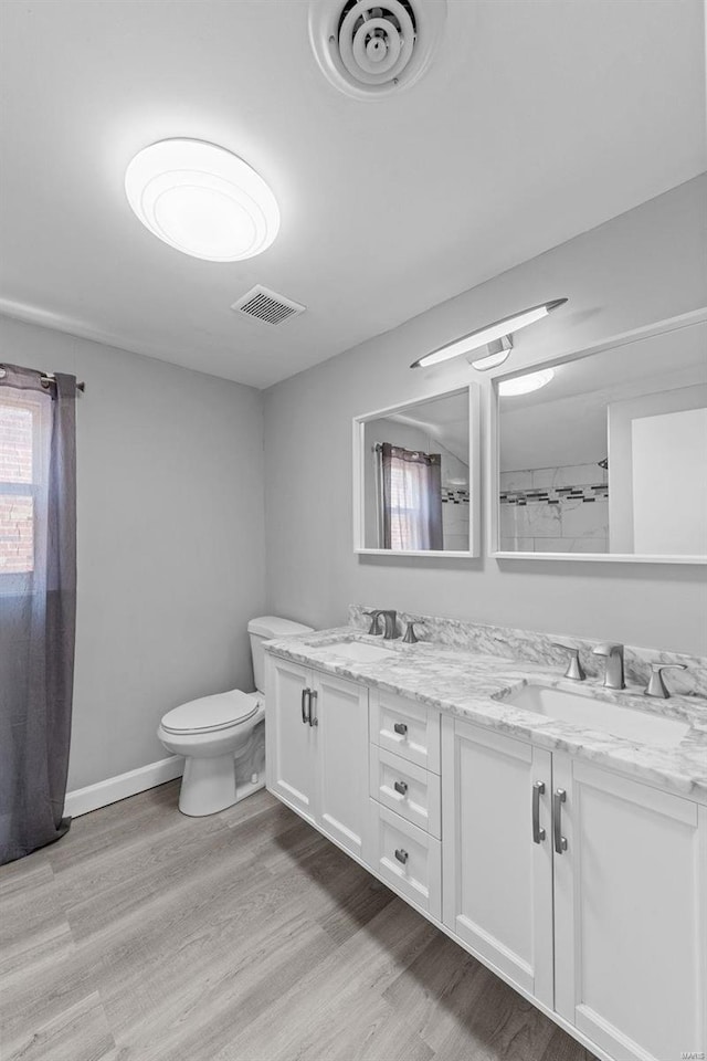 bathroom featuring wood finished floors, toilet, and double vanity
