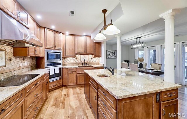 kitchen with stainless steel appliances, ornate columns, a sink, under cabinet range hood, and light wood-style floors