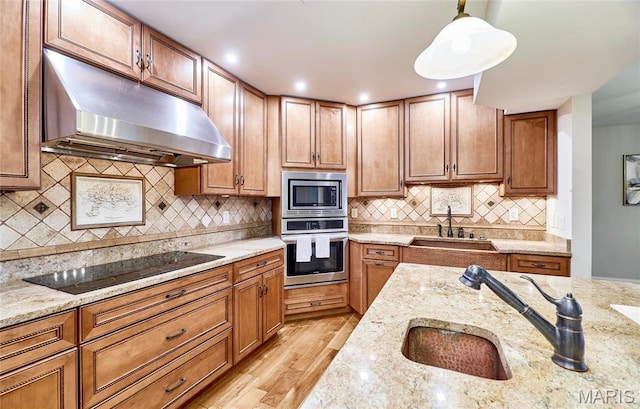 kitchen featuring stainless steel appliances, a sink, under cabinet range hood, and light wood-style floors