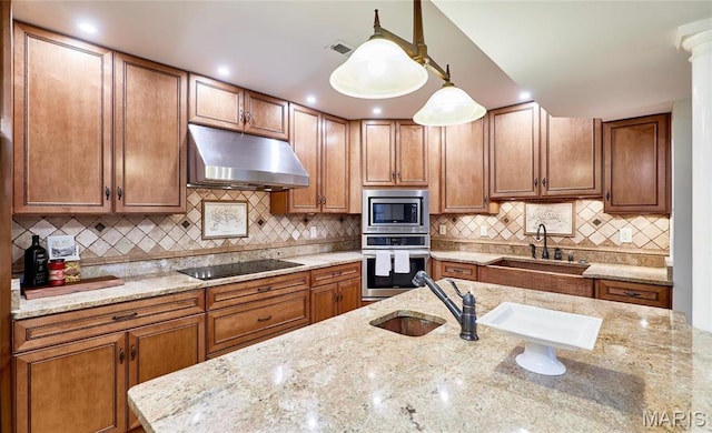 kitchen with stainless steel appliances, under cabinet range hood, a sink, and brown cabinets