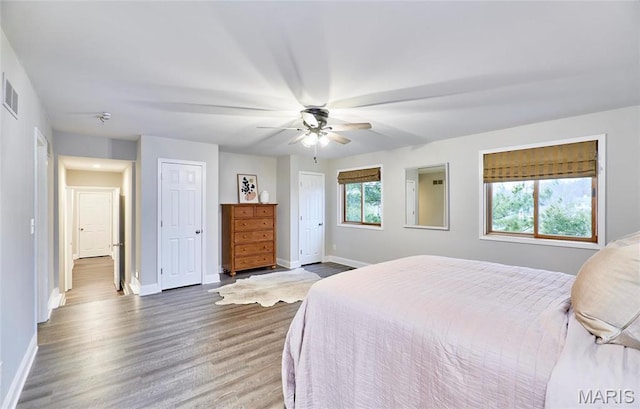 bedroom with baseboards, wood finished floors, multiple closets, and ceiling fan