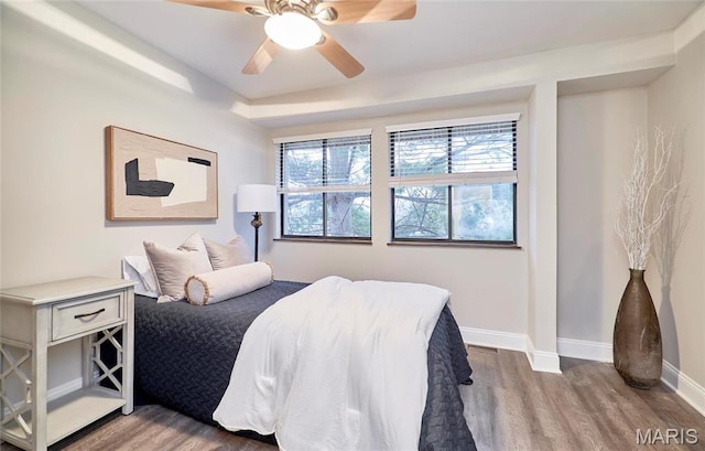bedroom with wood finished floors, baseboards, multiple windows, and ceiling fan