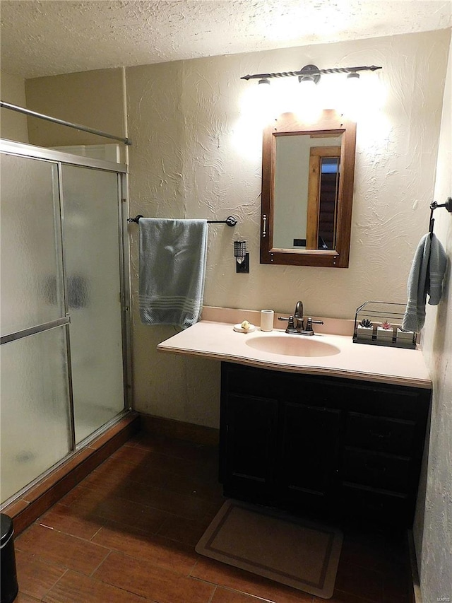bathroom with a textured ceiling, a shower stall, wood finished floors, vanity, and a textured wall