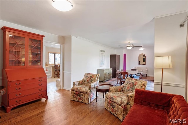 living area featuring a ceiling fan, ornamental molding, wood finished floors, and baseboards