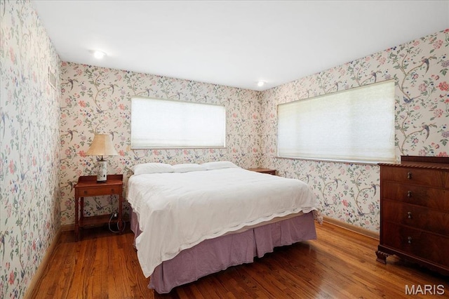 bedroom featuring wood finished floors, wallpapered walls, and baseboards