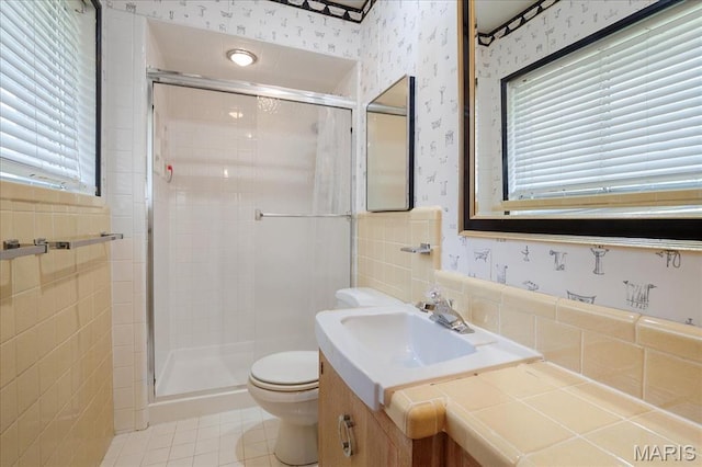 bathroom featuring wallpapered walls, tile patterned flooring, a stall shower, tile walls, and toilet