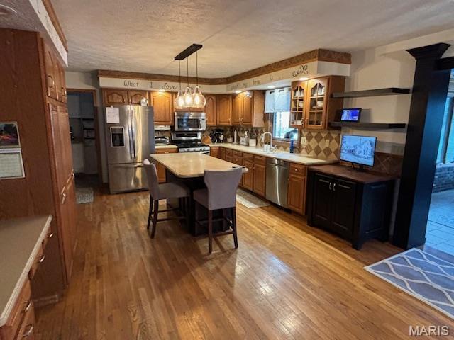 15020 Jamestown Rd, Breese, IL 62230 - kitchen featuring appliances with stainless steel finishes, brown cabinetry, hardwood / wood-style flooring, a breakfast bar area, and glass insert cabinets