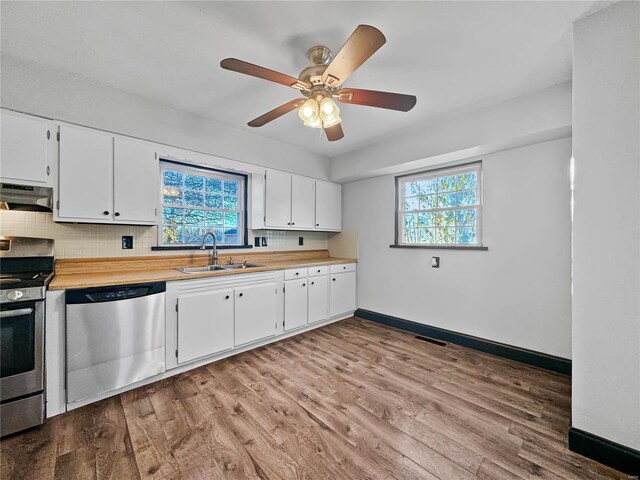 kitchen featuring appliances with stainless steel finishes, under cabinet range hood, a sink, wood finished floors, and baseboards