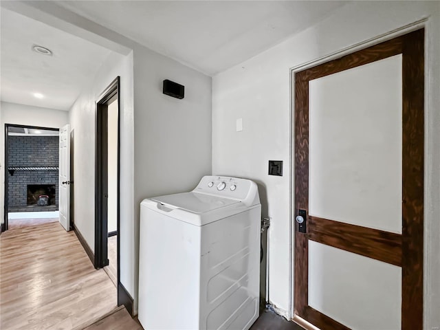 washroom with washer / clothes dryer, a brick fireplace, and light wood-type flooring