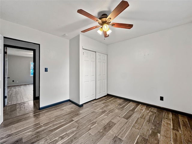 unfurnished bedroom featuring wood finished floors, a closet, baseboards, and ceiling fan