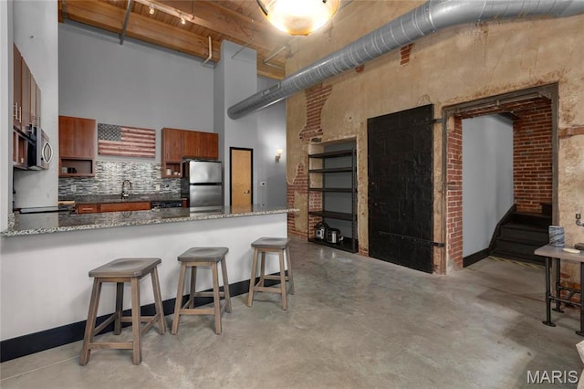 1113 Washington Ave Unit 215, Saint Louis, MO 63101 - kitchen featuring a towering ceiling, appliances with stainless steel finishes, brown cabinets, concrete floors, and a kitchen bar
