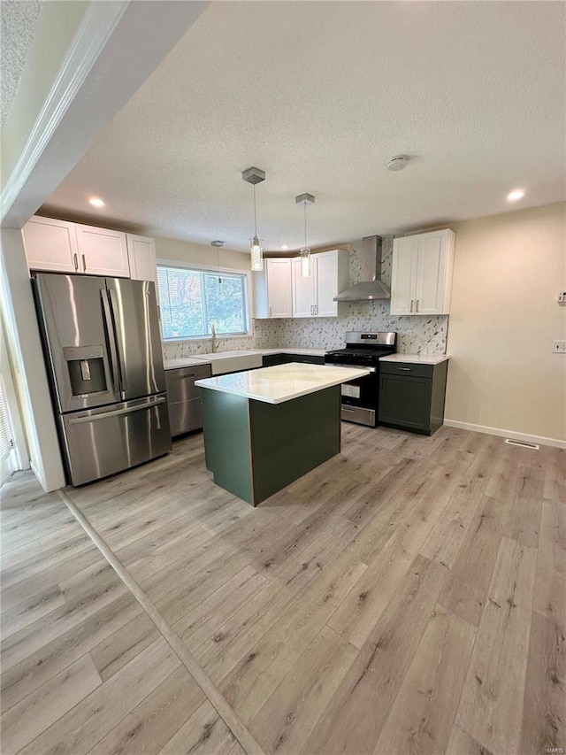 926 Justice Ct, Florissant, MO 63034 - kitchen featuring stainless steel appliances, wall chimney exhaust hood, light wood finished floors, white cabinets, and a textured ceiling