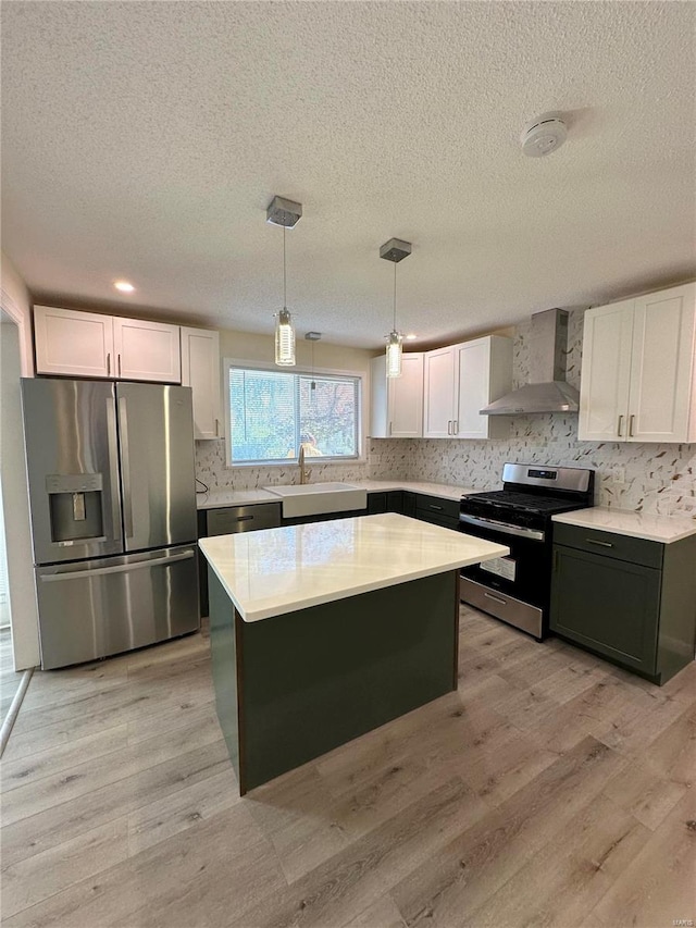 926 Justice Ct, Florissant, MO 63034 - kitchen featuring stainless steel appliances, wall chimney range hood, a sink, white cabinets, and a textured ceiling