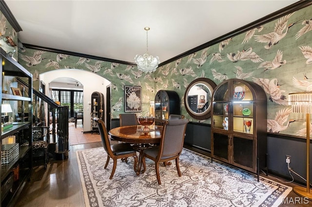 dining space featuring arched walkways, wallpapered walls, a chandelier, wood finished floors, and crown molding