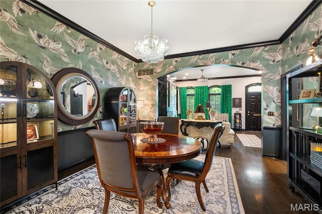 dining space featuring wallpapered walls, crown molding, wood finished floors, a chandelier, and arched walkways